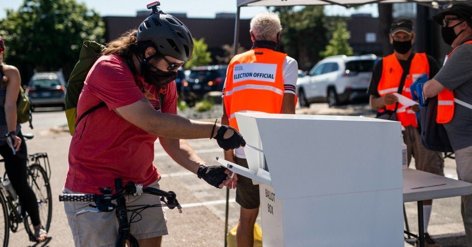 A voter on bicycle drops off their ballot at a drive through drop-off for absentee ballots on August 11, 2020 in Minneapolis, Minnesota.
